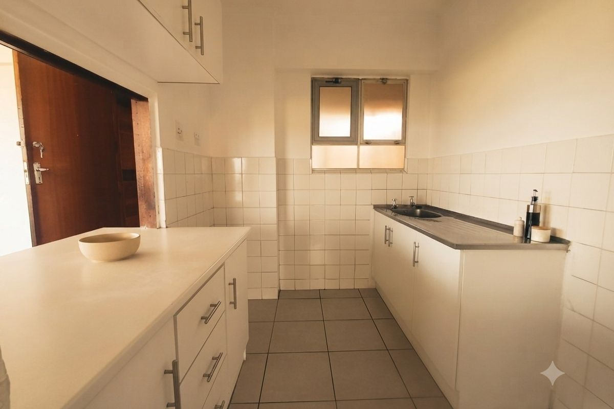 A functional kitchen featuring white built-in cabinetry, a stainless steel sink, tiled splashbacks, and neutral floor tiles.
