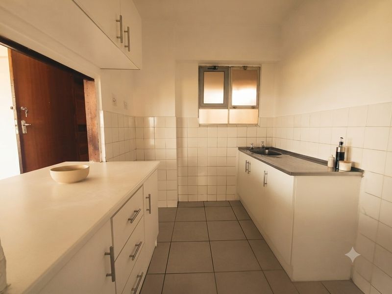 A functional kitchen featuring white built-in cabinetry, a stainless steel sink, tiled splashbacks, and neutral floor tiles.