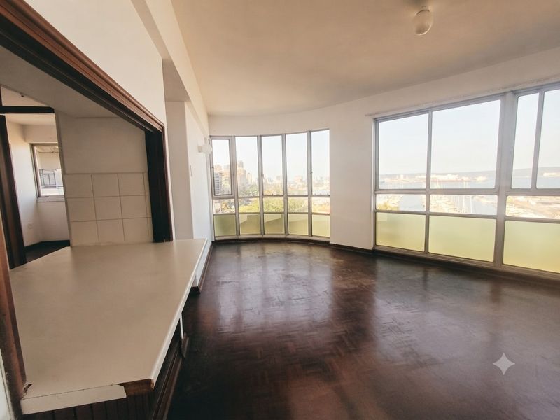 Spacious open-plan living area featuring parquet flooring, a breakfast counter, and expansive windows offering panoramic city and harbor views.