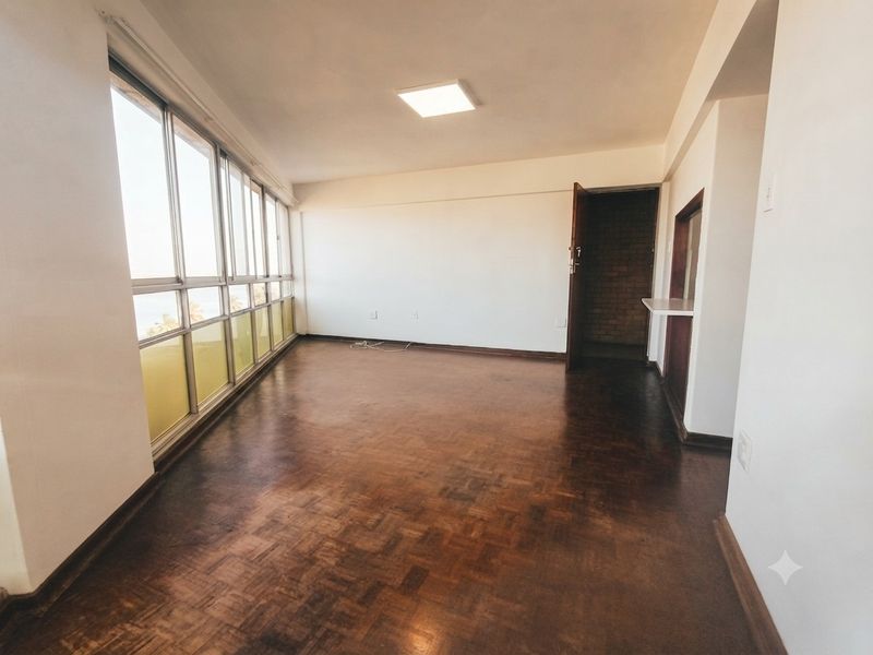 Spacious, empty living area featuring classic parquet flooring, large windows providing natural light, and a convenient built-in breakfast bar.