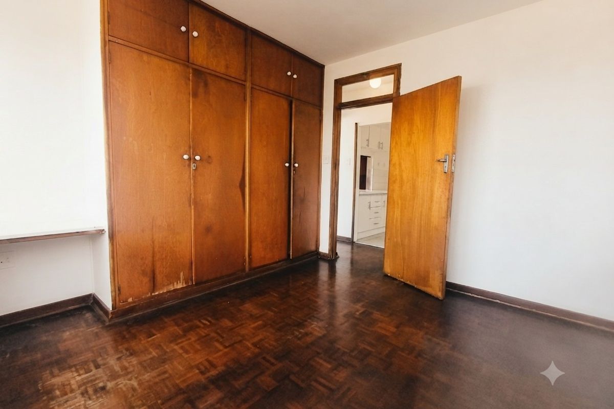 An empty bedroom featuring classic parquet flooring and extensive built-in wooden cabinetry, offering a neutral canvas for personalization.
