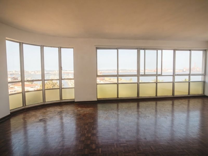 Spacious, empty living area featuring original parquet flooring and expansive windows offering panoramic harbour and city views.