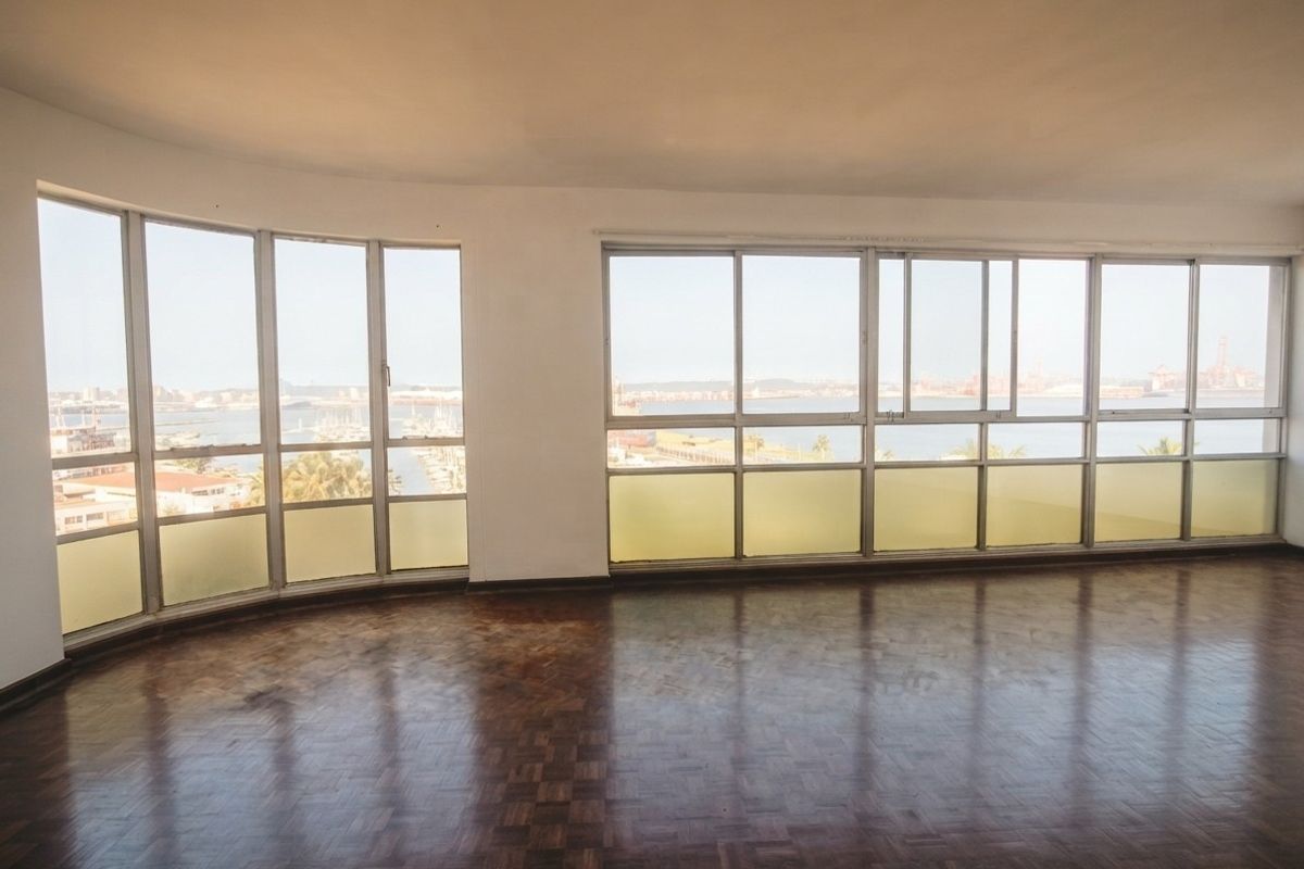 Spacious, empty living area featuring original parquet flooring and expansive windows offering panoramic harbour and city views.