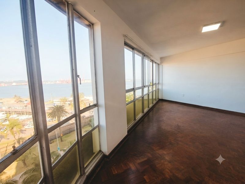 Spacious, empty living area featuring original parquet flooring and expansive windows offering panoramic coastal and harbor views.