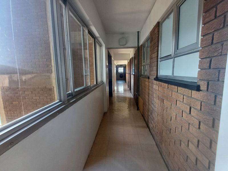 A long apartment hallway featuring exposed brick walls, tiled flooring, and aluminium-framed windows along the corridor.