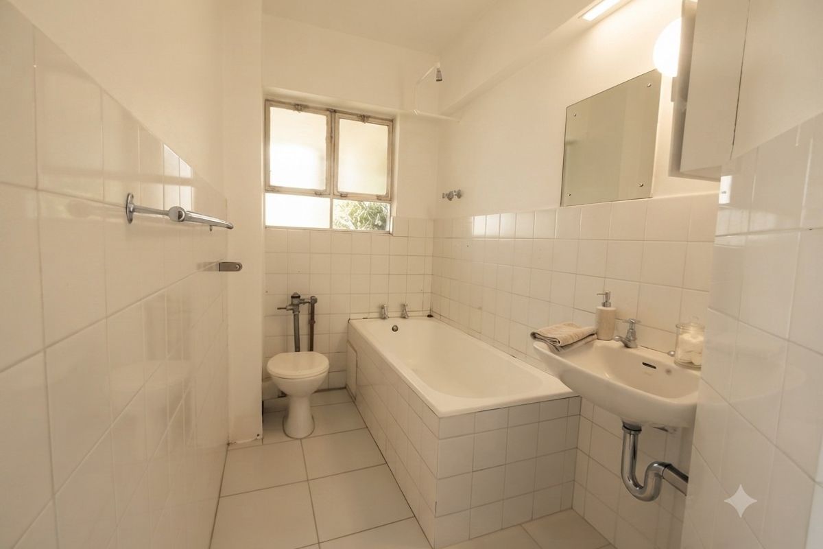 A functional bathroom featuring a bathtub, wall-mounted basin, and toilet with classic white tiled finishes throughout.