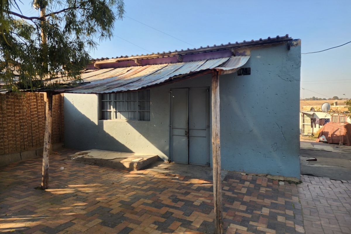 Rear exterior view of the property featuring a paved patio area covered by a corrugated iron roof structure supported by timber posts.