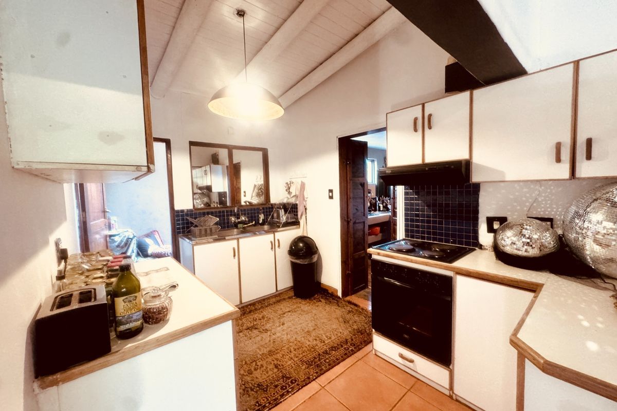 A dated kitchen featuring white cabinetry, electric cooking appliances, tiled splashbacks, and exposed timber ceiling beams.