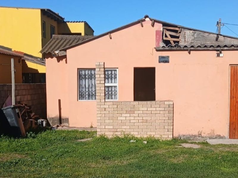 Rear view of a single-story house showing a small yard, brick boundary wall, and visible structural damage to the roofline and exterior facade.
