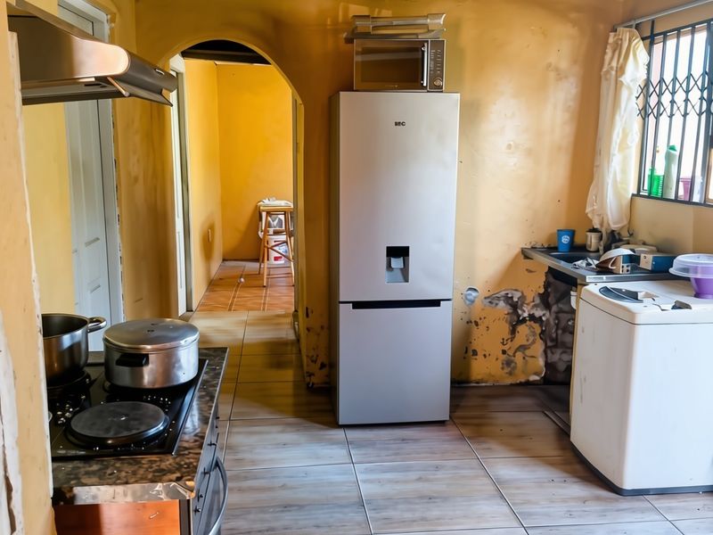 A dated kitchen featuring tiled floors, a timber ceiling, and built-in cooking appliances, currently showing significant wall surface deterioration and peeling paint.