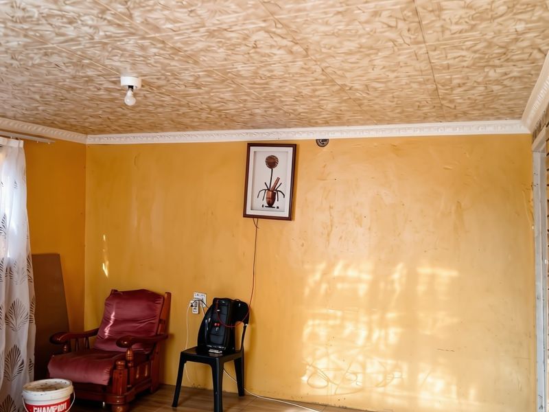 A living room featuring tiled flooring, textured ceiling tiles, and decorative cornice, requiring cosmetic updates to the wall finishes and electrical presentation.