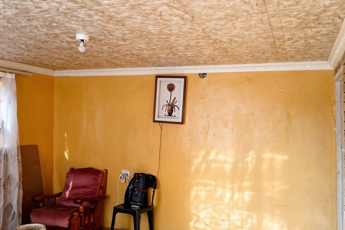A living room featuring tiled flooring, textured ceiling tiles, and decorative cornice, requiring cosmetic updates to the wall finishes and electrical presentation.