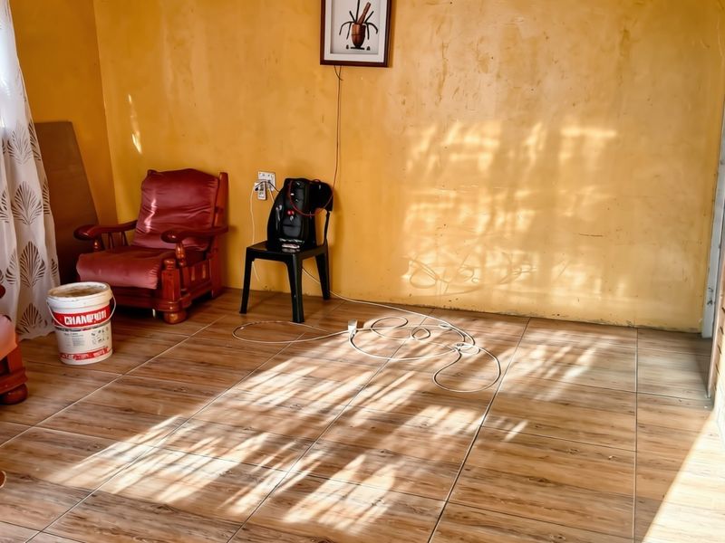 A living room area featuring wood-look tiled flooring and decorative ceiling cornicing, with yellow painted walls requiring cosmetic attention.
