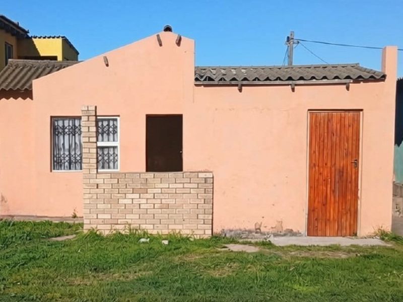 Rear exterior view of a single-story house featuring a peach-colored facade, corrugated roof tiles, and a wooden entrance door.