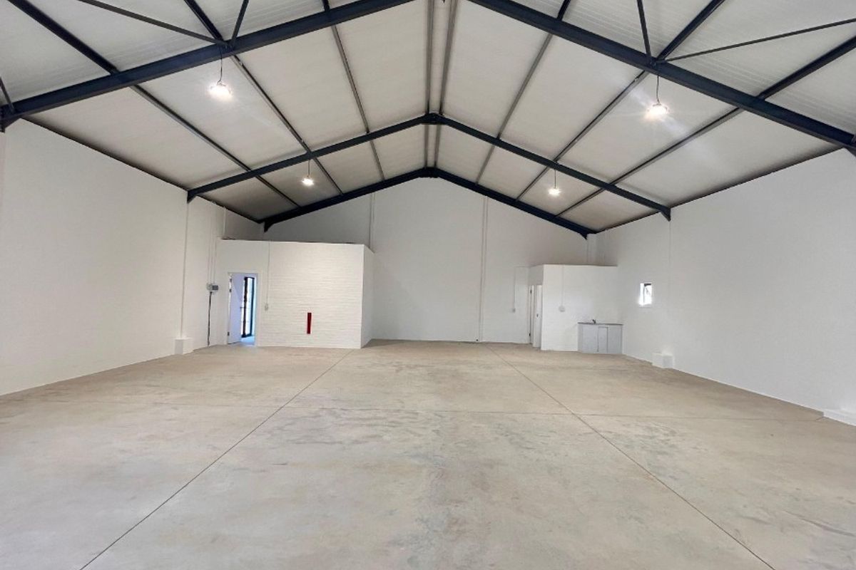 Spacious commercial warehouse or utility space featuring high exposed steel roof trusses, polished concrete flooring, and integrated partitioned office area.