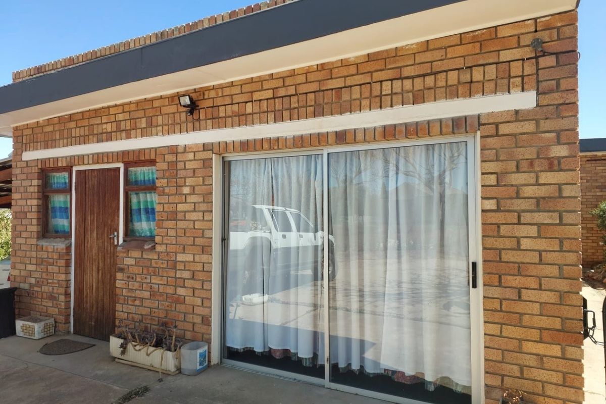 Rear exterior view of a face brick building featuring a sliding glass door, timber entrance door, and concrete patio area.