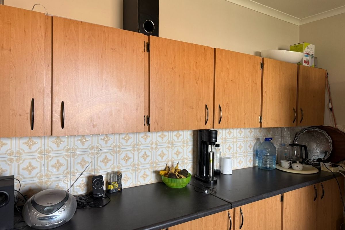 A functional kitchen area featuring wood-look laminate cabinetry, a dark countertop, and a decorative ceramic tile backsplash.