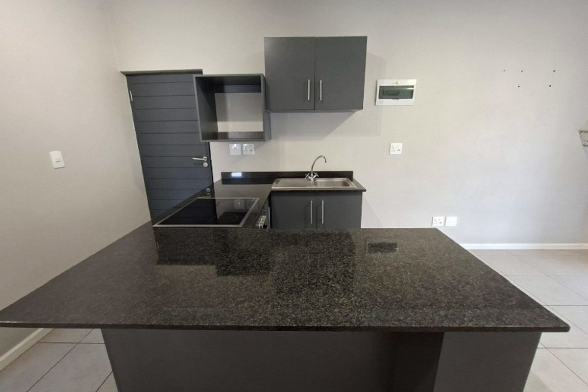Modern kitchen featuring dark grey cabinetry, granite countertops, an integrated electric hob, and tiled flooring in an open-plan layout.