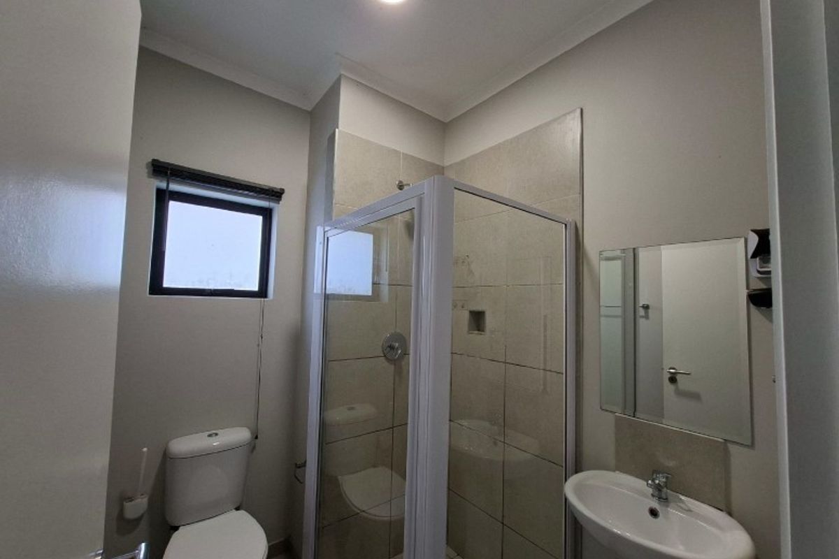 A clean, functional bathroom featuring a glass-enclosed shower, pedestal basin, and toilet with neutral wall tiling.