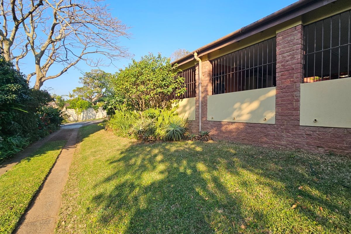 A view of the rear exterior featuring a brick facade with security bars, a concrete pathway, and a well-maintained garden area.