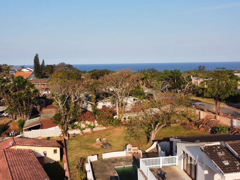 Aerial view of the property showing the backyard, swimming pool, patio area, and surrounding neighbourhood with a distant ocean view.