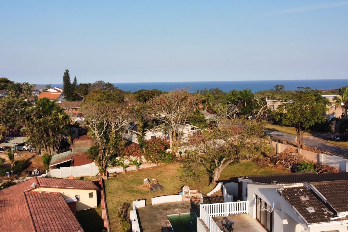 Aerial view of the property showing the backyard, swimming pool, patio area, and surrounding neighbourhood with a distant ocean view.