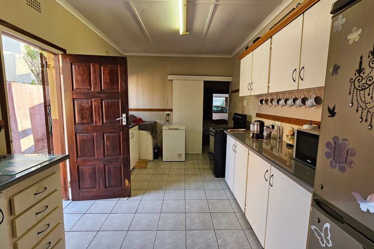 A functional kitchen featuring tiled flooring, laminate countertops, and white cabinetry, with direct access to an outdoor area via a wooden door.