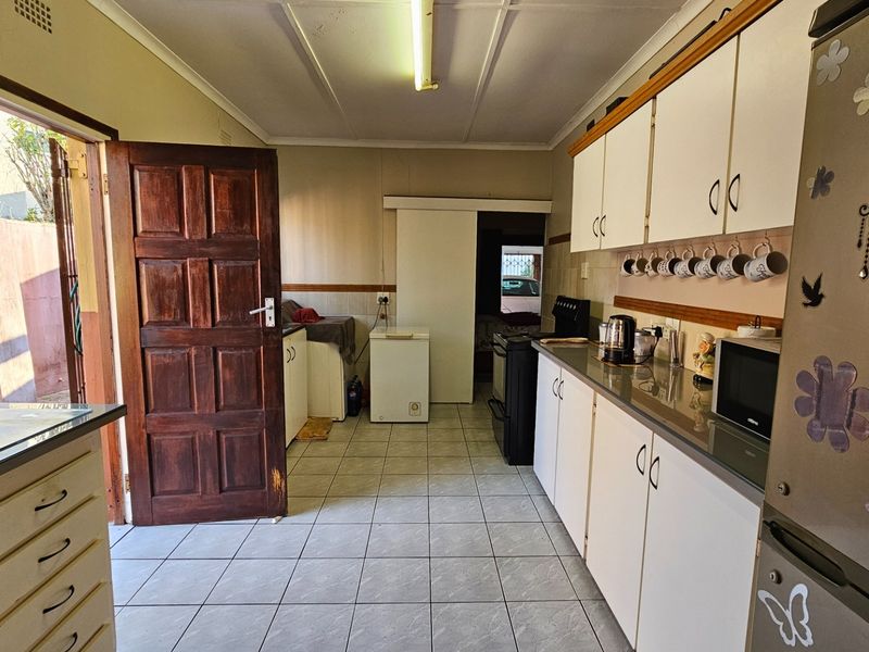 A functional kitchen featuring tiled flooring, laminate countertops, and white cabinetry, with direct access to an outdoor area via a wooden door.