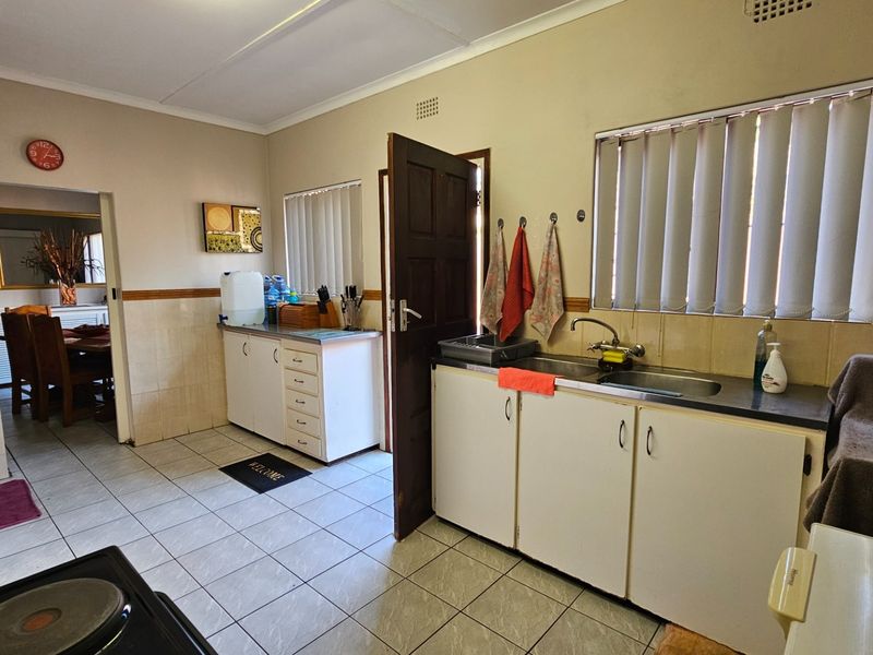 A functional kitchen featuring tiled flooring, built-in cabinetry, and a double basin stainless steel sink, with direct access to the adjacent dining area.