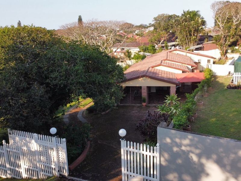Aerial view of the property featuring a paved driveway, carport, and white picket fencing surrounding the landscaped garden area.