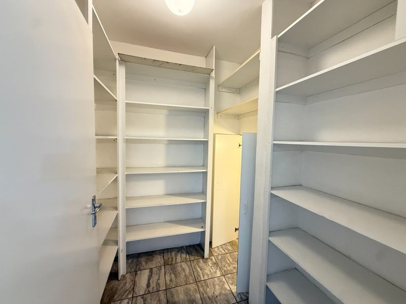 A functional walk-in pantry or scullery area featuring extensive built-in white shelving and durable tiled flooring.