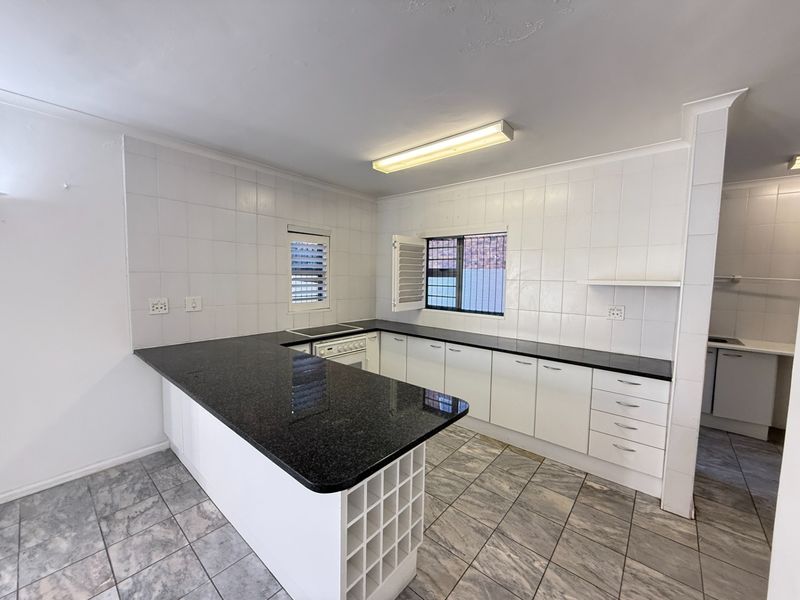 A functional kitchen featuring white cabinetry, black granite countertops, a built-in oven and hob, and tiled flooring throughout.