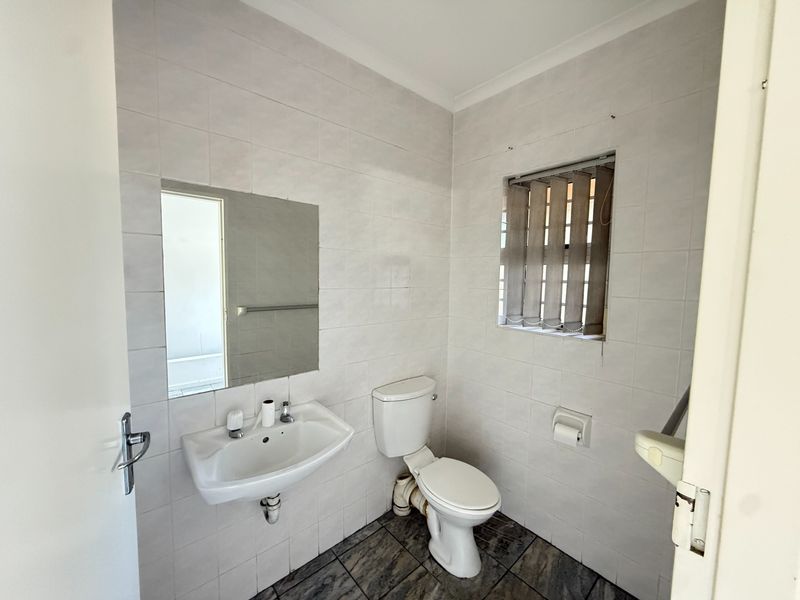 A functional bathroom featuring tiled walls and flooring, a wall-mounted basin, and a standard toilet, presenting a clean but dated aesthetic.