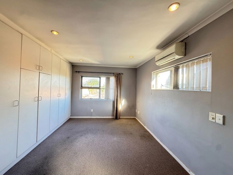 A spacious, empty bedroom featuring built-in cupboards, a split-system air conditioner, and recessed downlights, offering a neutral canvas for personalization.