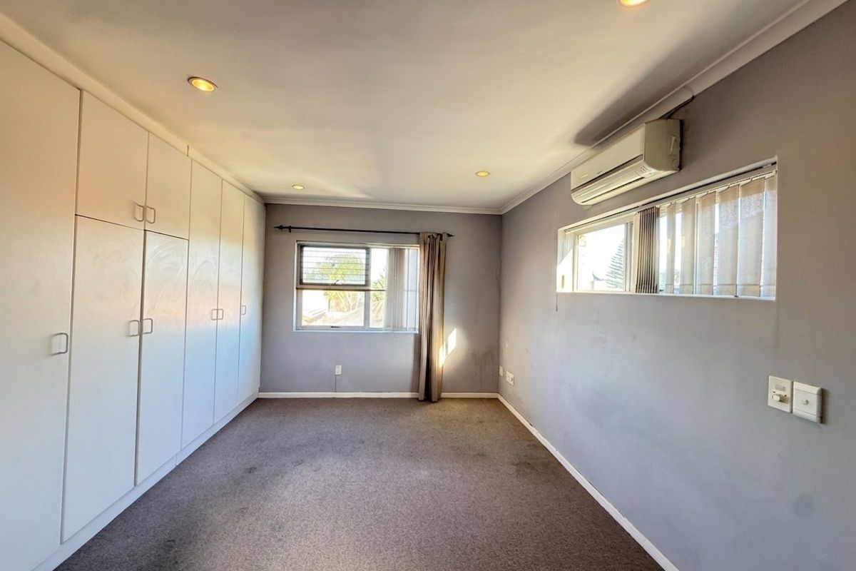 A spacious, empty bedroom featuring built-in cupboards, a split-system air conditioner, and recessed downlights, offering a neutral canvas for personalization.