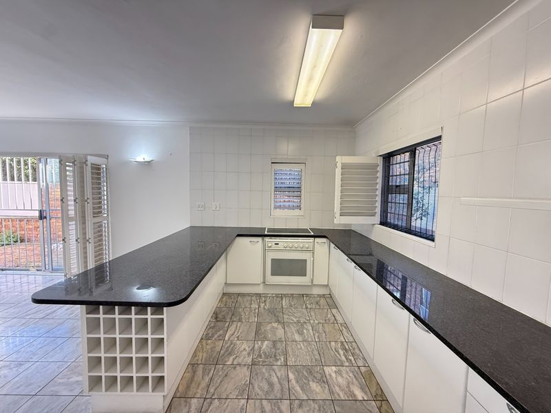 A spacious, empty kitchen featuring granite countertops, built-in oven and hob, tiled splashbacks, and a built-in wine rack, offering a clean canvas for updates.