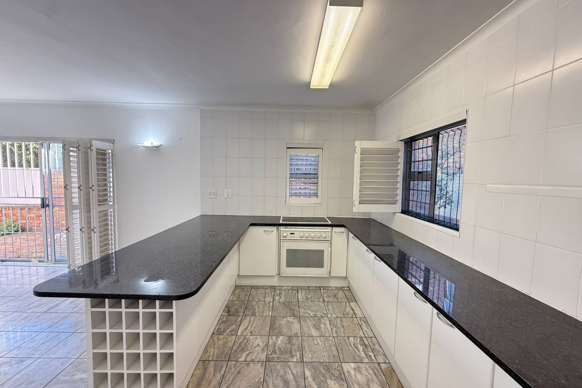A spacious, empty kitchen featuring granite countertops, built-in oven and hob, tiled splashbacks, and a built-in wine rack, offering a clean canvas for updates.