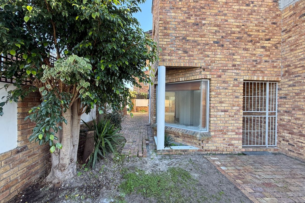 Rear exterior view of the property featuring a face brick facade, paved walkway, and a secure entrance gate.