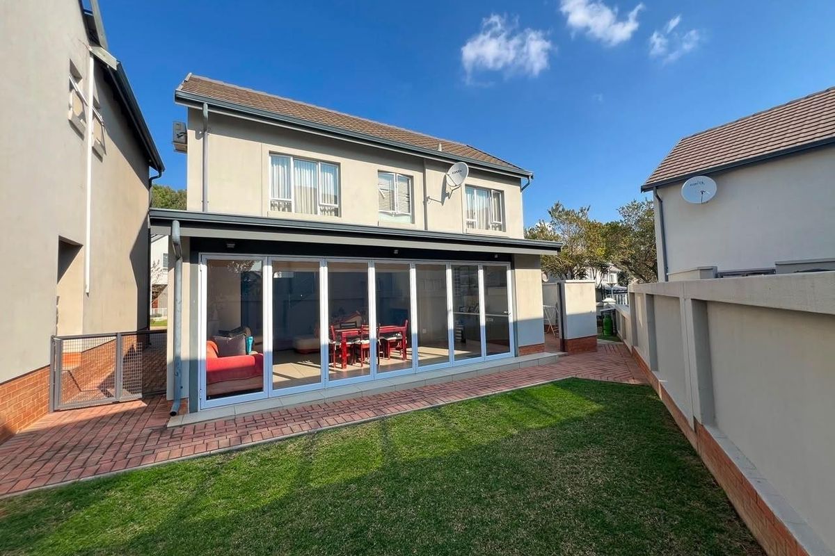 Rear view of the property featuring a paved patio area, a small lawn, and large bi-fold doors leading into the living space.