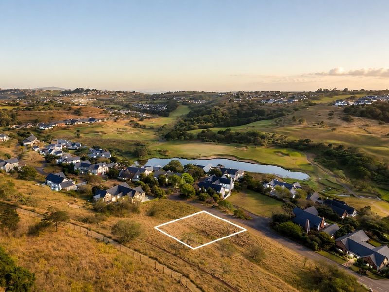 An aerial view of a vacant residential plot situated within a scenic estate, featuring surrounding landscape and nearby housing.