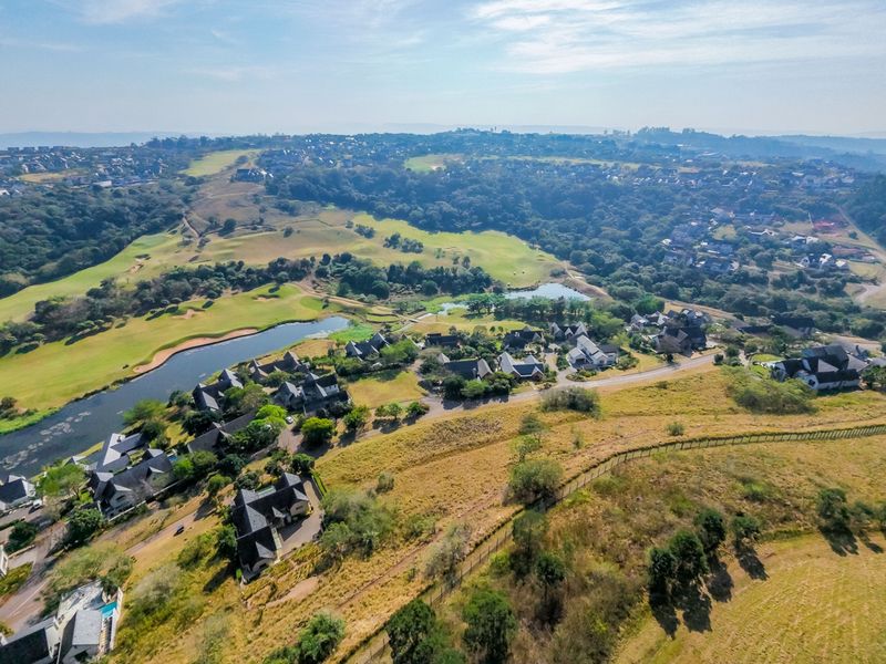 An aerial view of a residential estate featuring landscaped grounds, a golf course, and a lake in a scenic setting.
