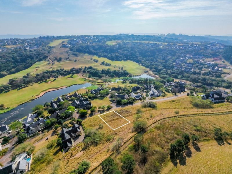 An aerial view of a vacant residential plot situated within a scenic estate, featuring surrounding greenery and established residential properties.