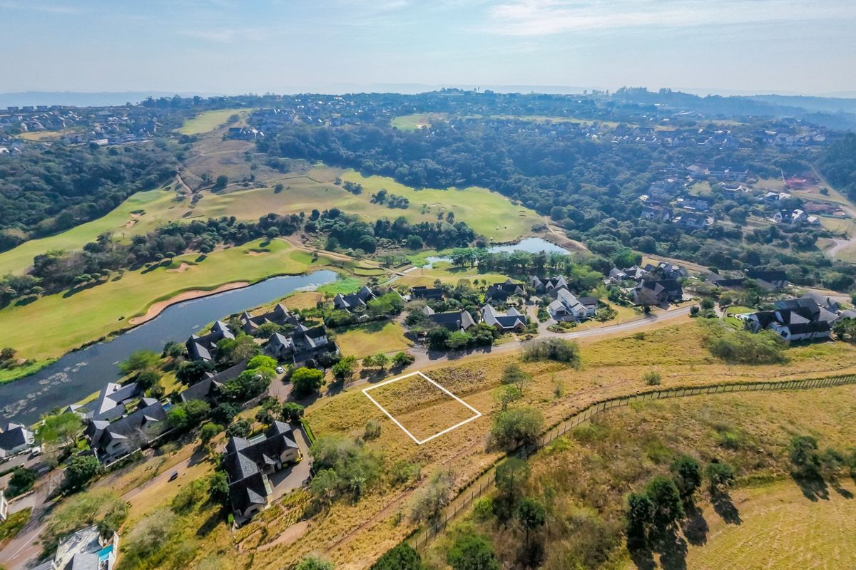 An aerial view of a vacant residential plot situated within a scenic estate, featuring surrounding greenery and established residential properties.