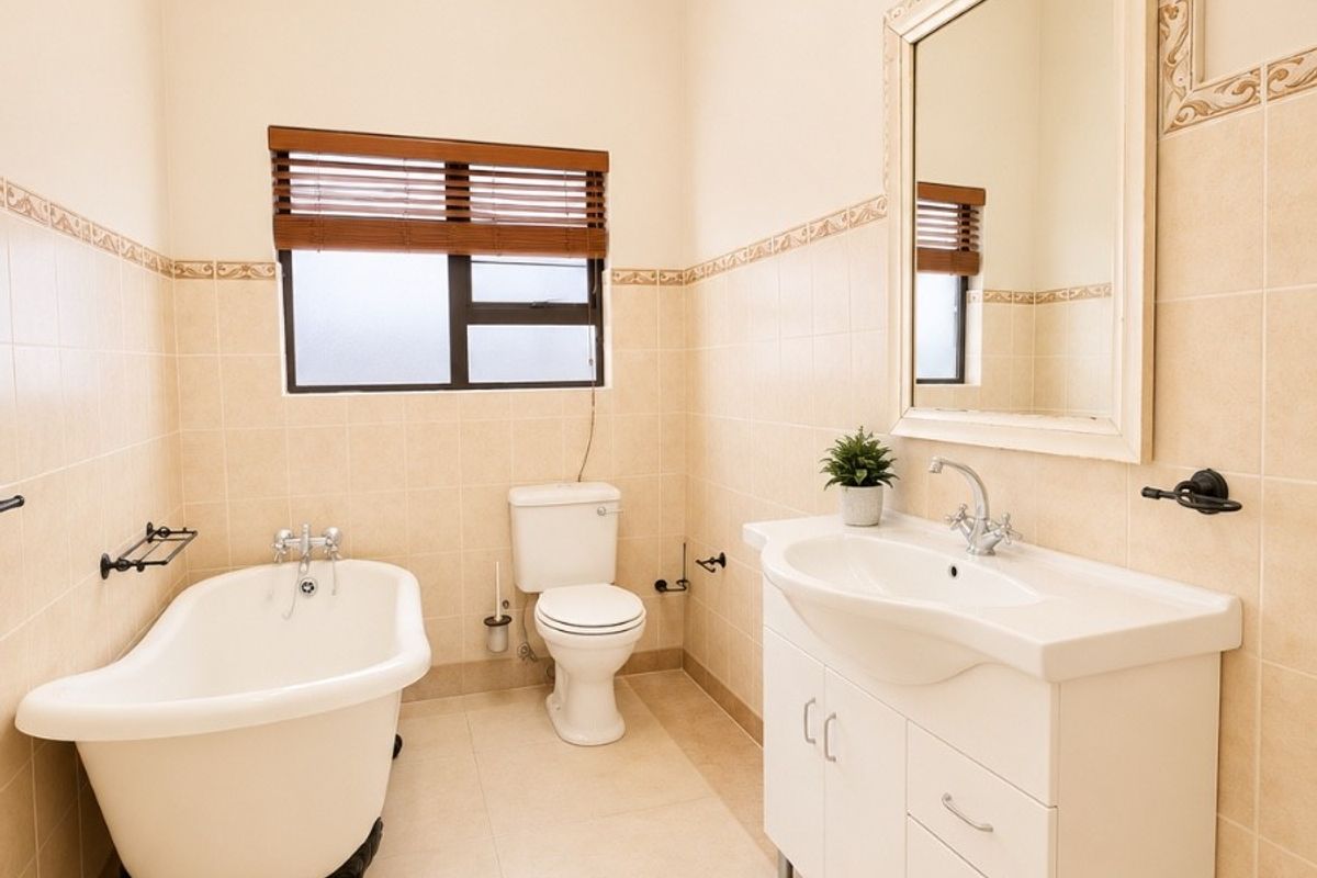 A well-maintained bathroom featuring a classic freestanding bathtub, a modern vanity unit with basin, and neutral wall and floor tiling.