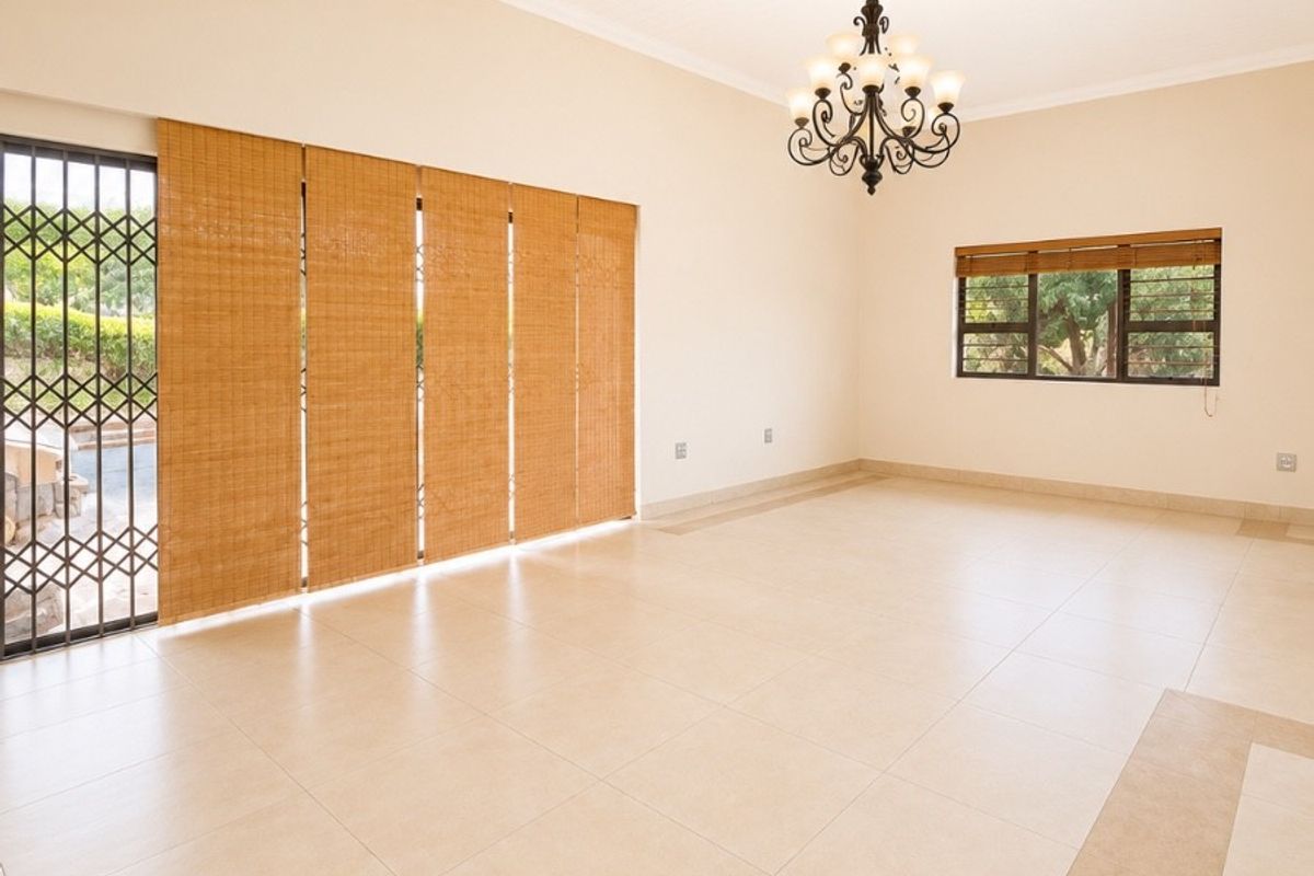 Spacious, light-filled living area featuring neutral tiled flooring, a classic chandelier, and secure sliding door access to the exterior.