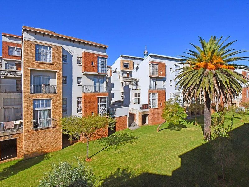 Exterior view of a multi-story apartment complex featuring brick facades, private balconies, and a well-maintained communal garden area.