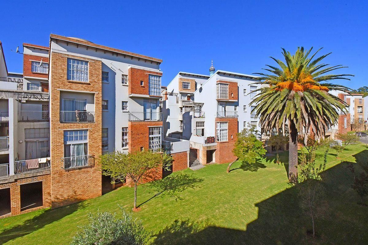 Exterior view of a multi-story apartment complex featuring brick facades, private balconies, and a well-maintained communal garden area.