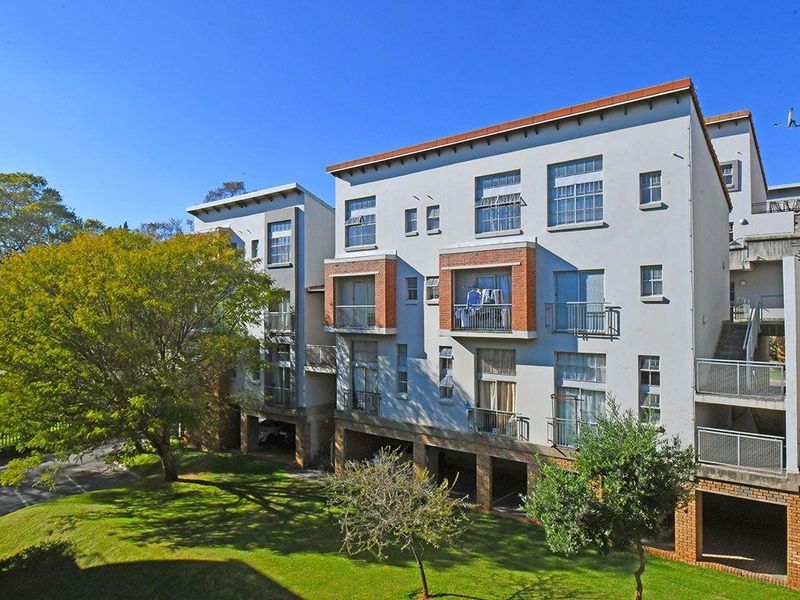 A view of the rear elevation of a multi-story apartment complex featuring balconies, brick detailing, and ground-level undercover parking areas.