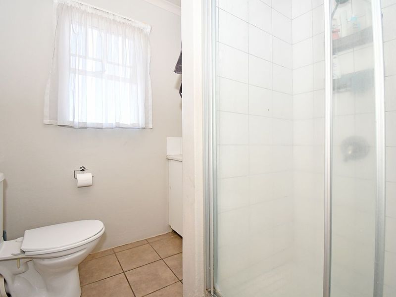A functional bathroom featuring a shower enclosure, toilet, and vanity cabinet with tiled flooring and a window for natural light.