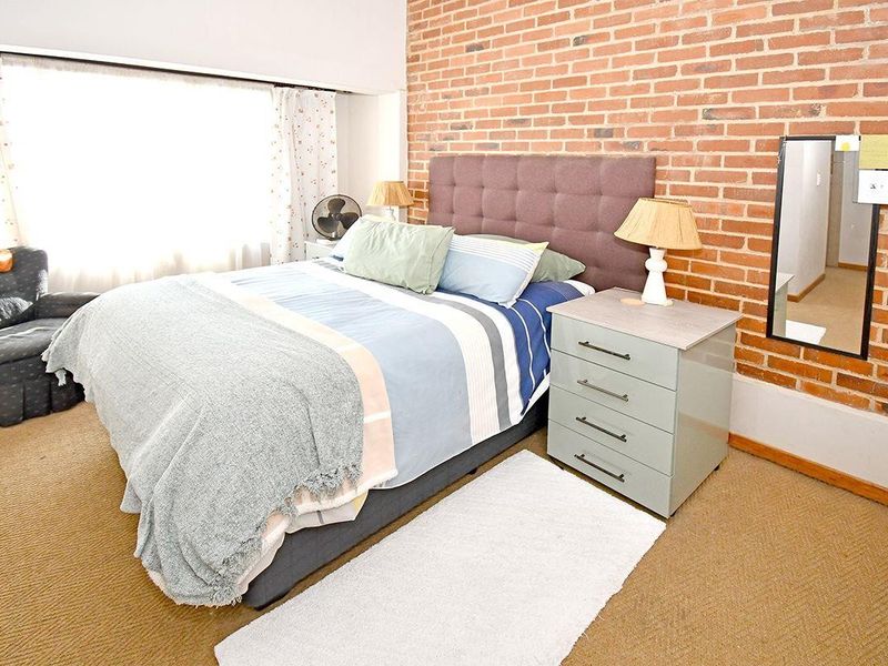 A bedroom featuring an exposed brick feature wall and carpeted flooring, offering a warm and textured aesthetic.